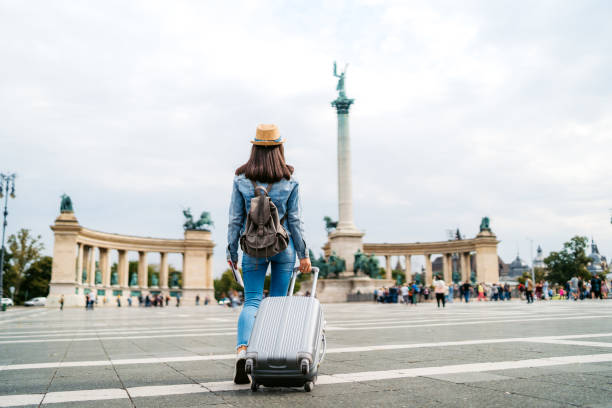 Young caucasian slim tourist woman visiting Budapest. Walking over Heroes' Square with luggage and map.