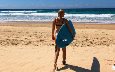 Student på stranden med sin surfbräda