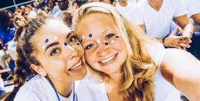 Två utbytesstudenter med färg i ansiktet är på en fotbollsmatch