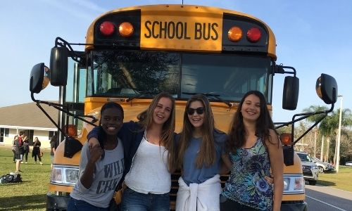 Fyra kvinnliga studenter poserar framför en skolbuss