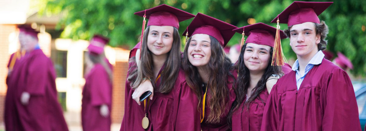 Fyra studenter tar examen och är klädda i lila kappa och hatt