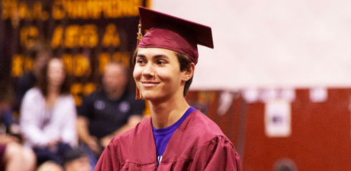 Porträtt av en manlig student i USA som tar examen. Iklädd vinröd kappa och mössa.