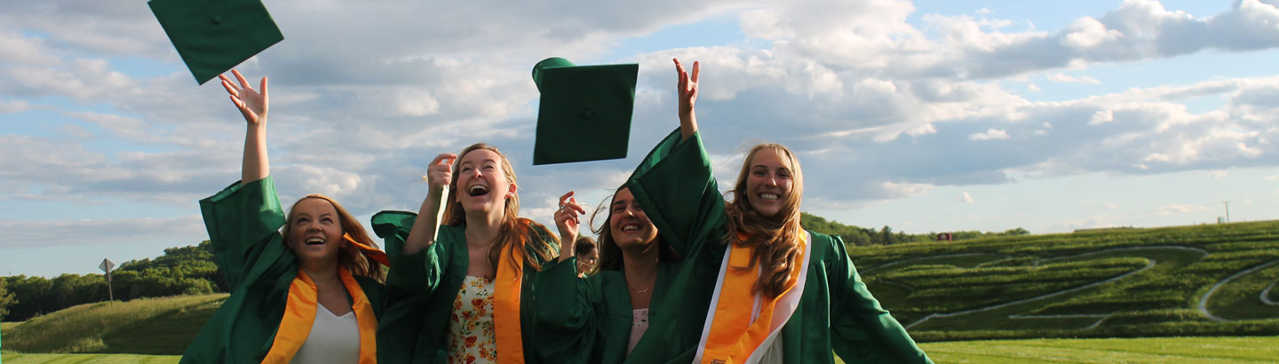 Studenter på examensdagen är klädda i gröna kappor och kastar sina hattar i luften