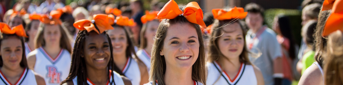 Leende cheerleaders i vitt med orange rosett i håret