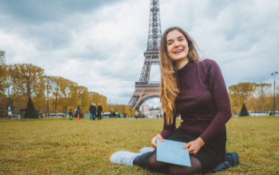 Student sitter på gräset med Eiffeltornet i bakgrunden.