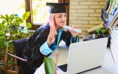 En student som precis tagit examen sitter vid datorn och visar upp sitt diplom.