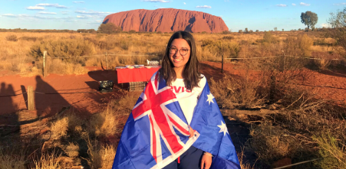 High school student poserar framför Red Rock i Australien med Australiens flagga virad om sig.