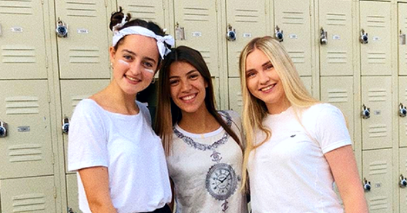Tre studenter i vita, sportiga kläder framför skåp.
