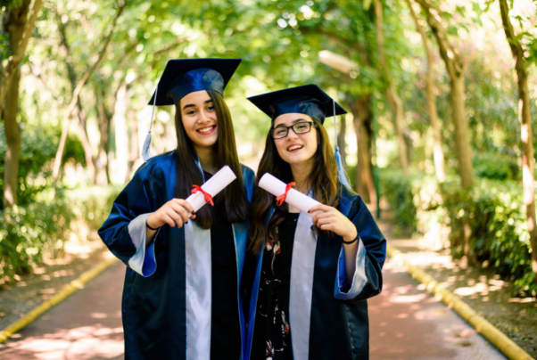Två studenter på examensdagen, klädda i blå kappa och hatt och håller i sina diplom.