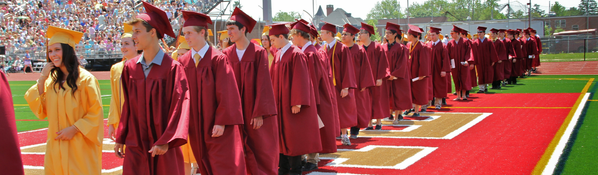 Många high school studenter på examensdagen går på ett led i sina vinröda kappor och hattar.