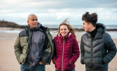 En utbytesstudent och hans värdfamilj promenerar på stranden på hösten