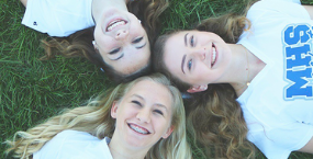 Tre tjejer liggande på marken med huvuden ihop och skrattar